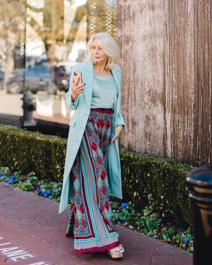 Woman wearing a seafoam overcoat with a silk cami and print palazzo pants  