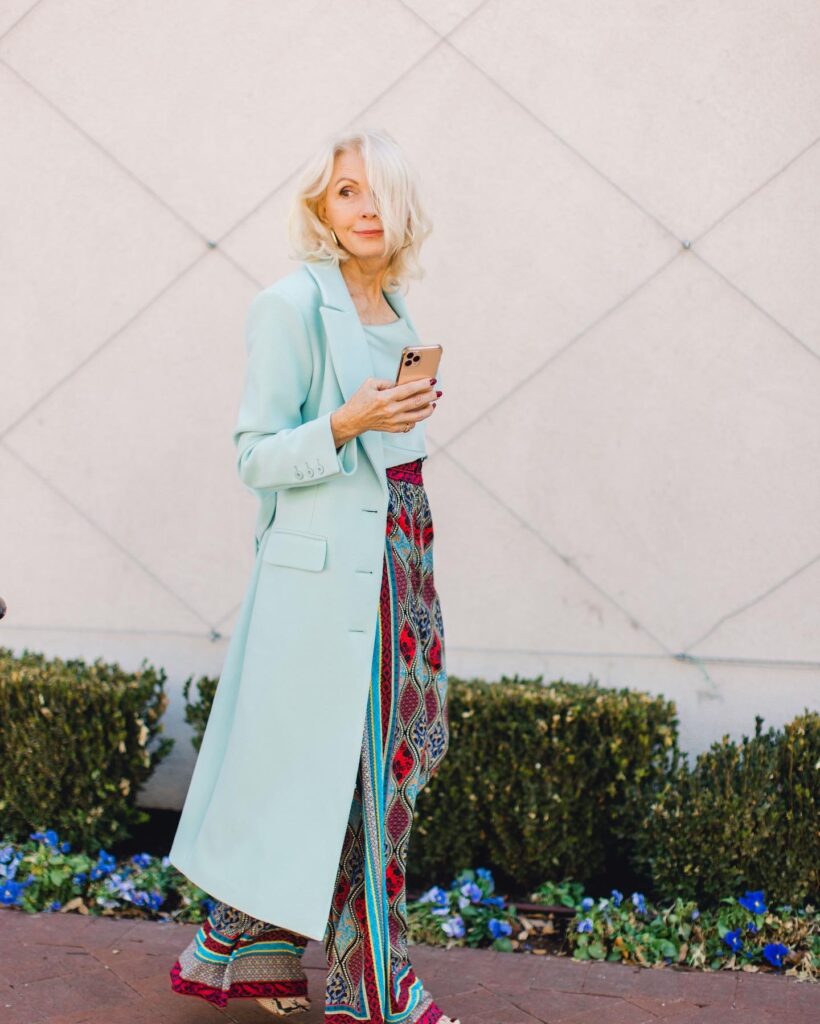 Woman wearing a seafoam overcoat with a silk cami and print palazzo pants  for the spring travel capsule wardrobe edit with Alice and Olivia