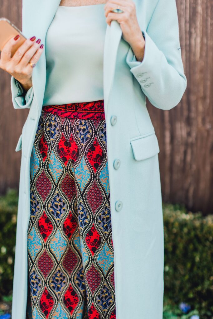 Woman wearing a seafoam overcoat with a silk cami and print palazzo pants  for the spring travel capsule wardrobe edit with Alice and Olivia