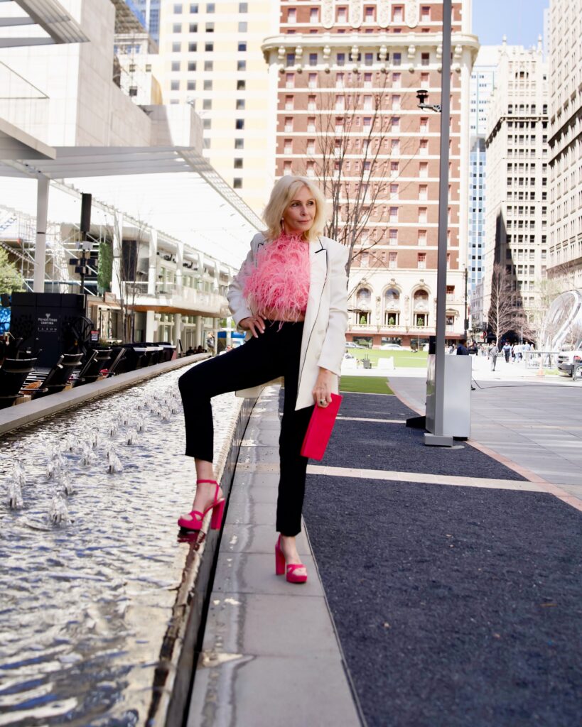 Sonia, urban environment with high red platform heels, feather crop top, with white blazer and black pants. With red clutch.