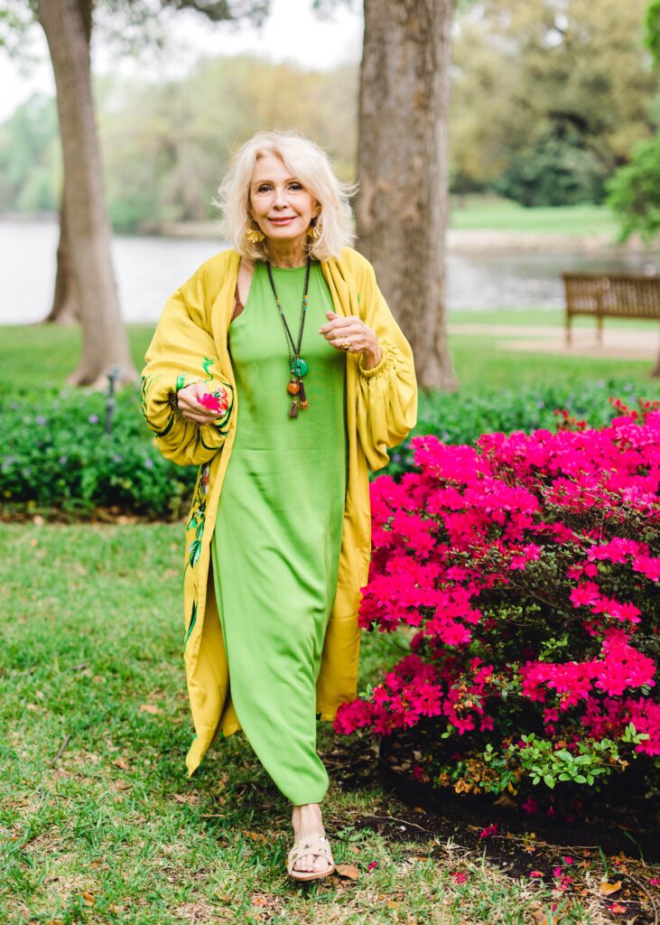 standing in park with pink shrubs in background wearing yellow kimono with green slip dress