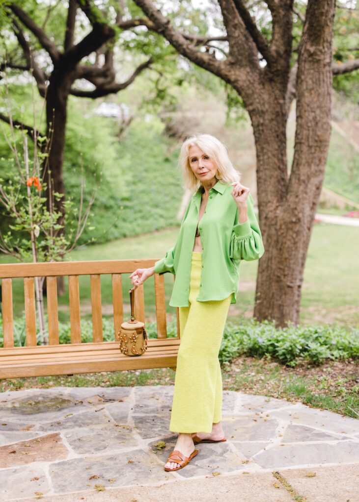 wearing green shirt and pants with brown handbag on garden bench