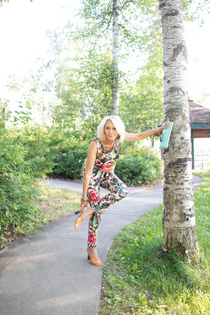 Sonia in spring all-floral sleeveless jumpsuit and slip on yellow sandals.