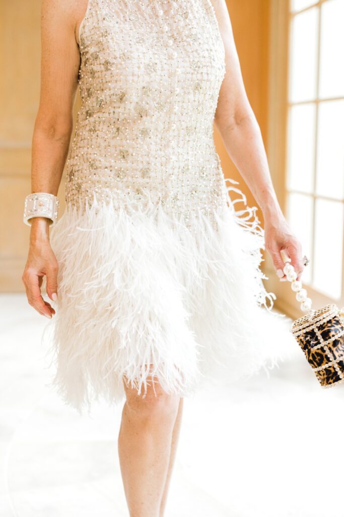 beaded sheath dress with white ostrich feathers carrying a handbag 