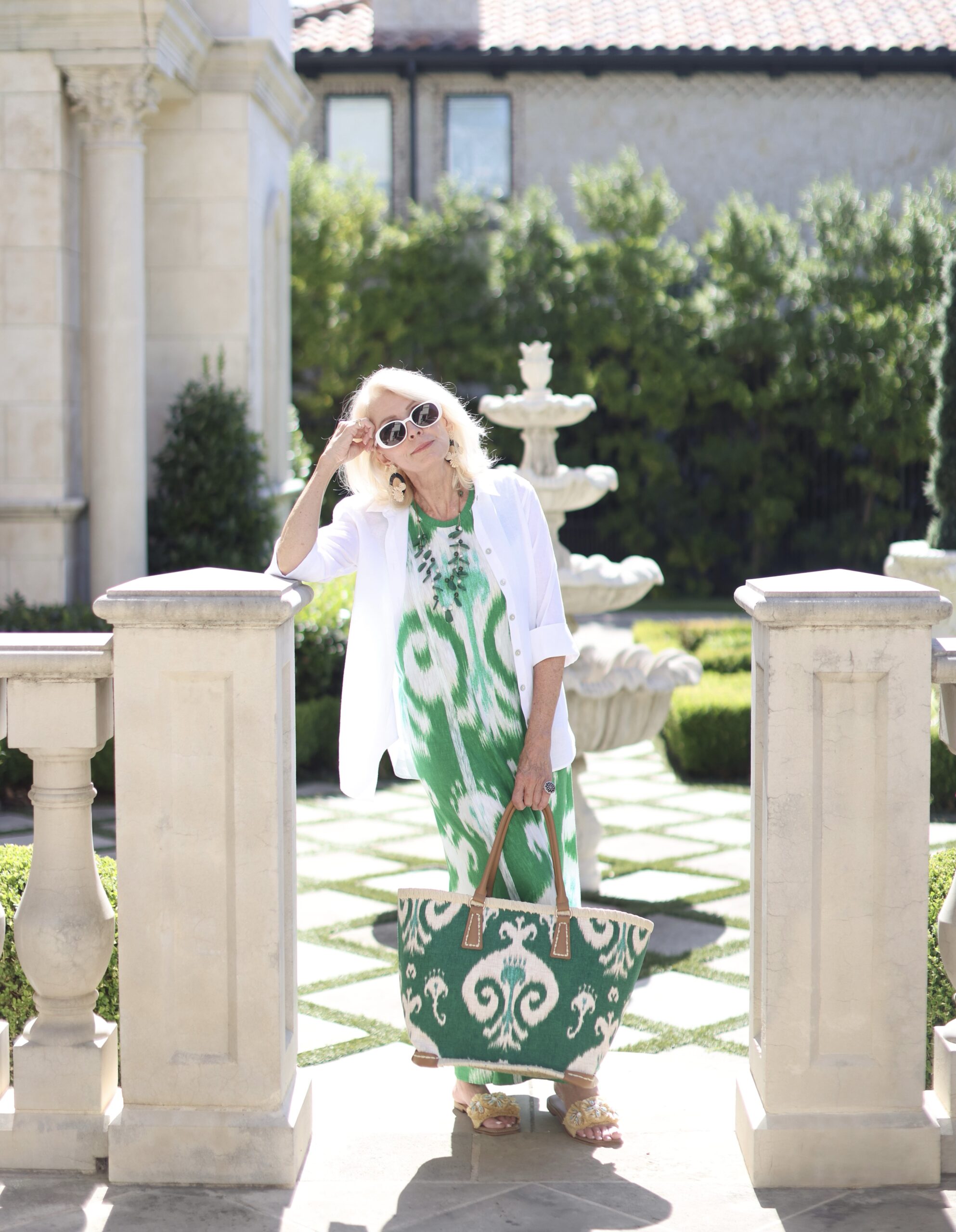 Woman leaning on pillar holding a green printed tote bag and wearing a green ikat printed dress