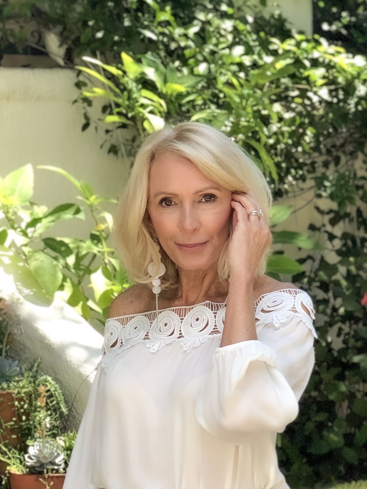 Smiling woman looking at the camera wearing white top and earrings and the best sunblock