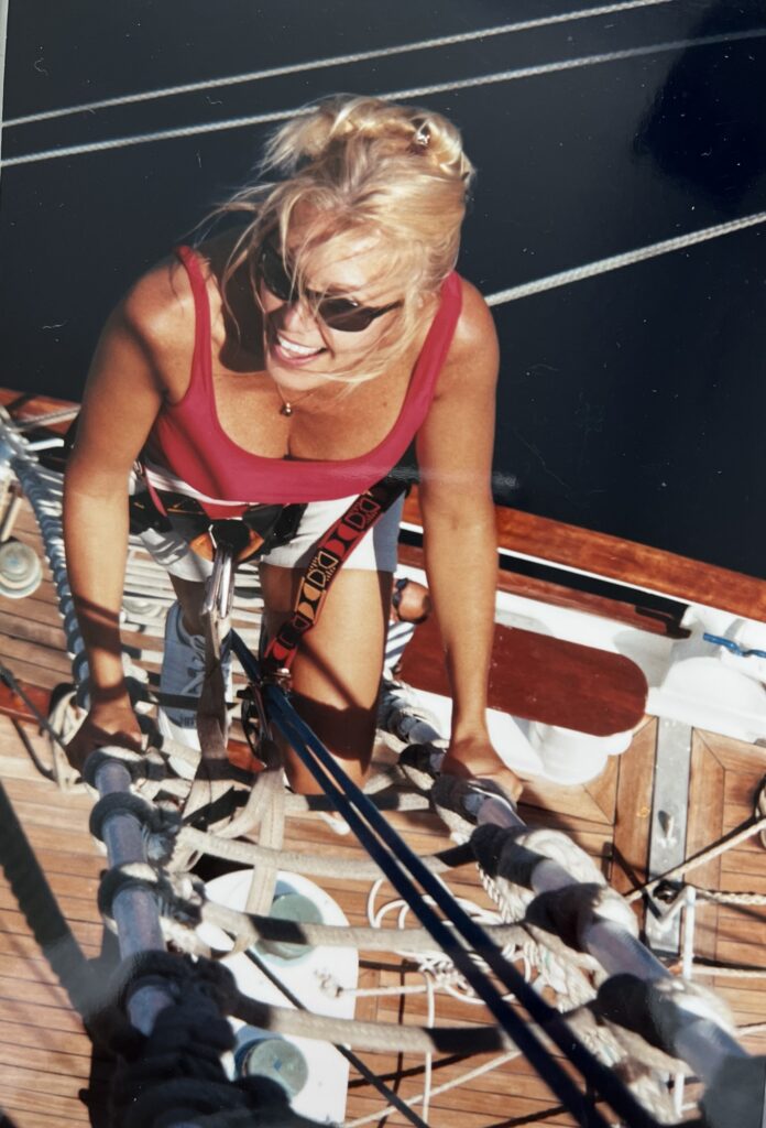 Smiling blonde woman wearing black sunglasses climbing a ladder on a boat