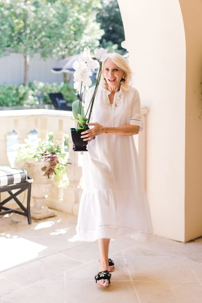 Style beyond age wearing white summer fashion dress holding a potted plant