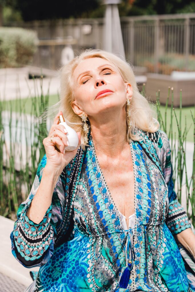 Woman basking in the sun in a blue dress holding a white spritzer bottle wearing best sunblock