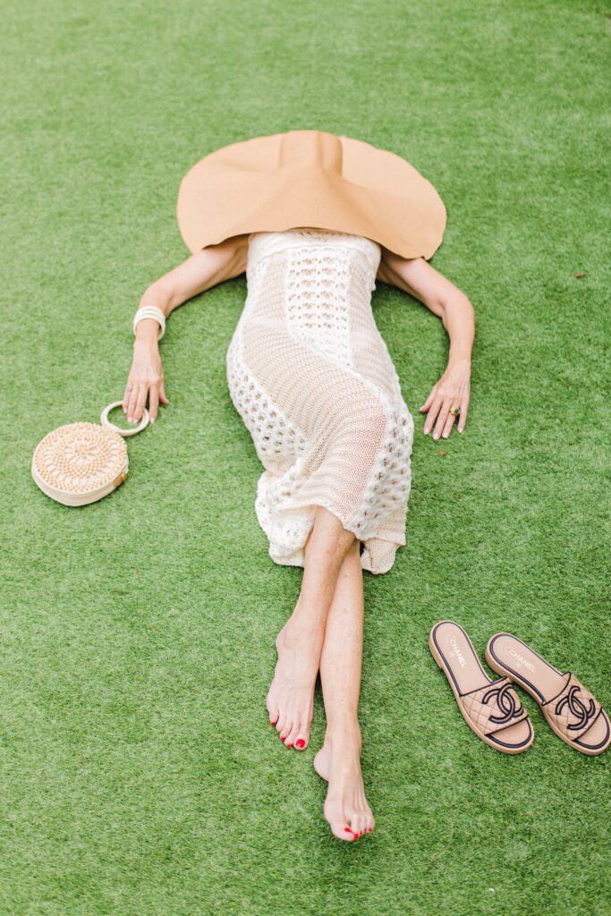 Style Beyond Age laying down in a summer neutrals crochet dress and big hat