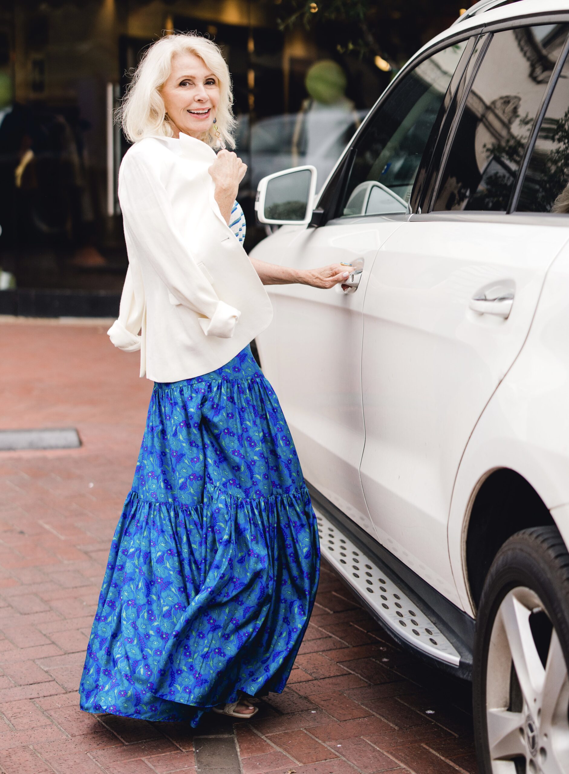Happy woman posing next to a white SUV Wearing a blue top and skirt