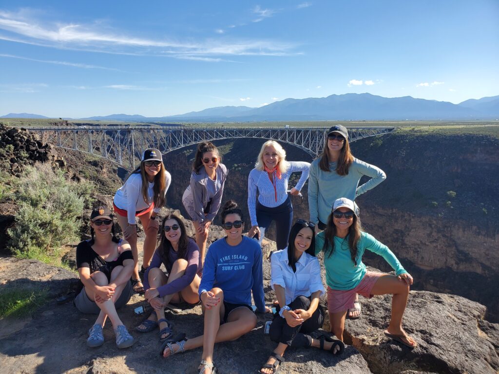 Group of women standing near a cliff, posing in front of the Gorge Bridge in Taos, New Mexico