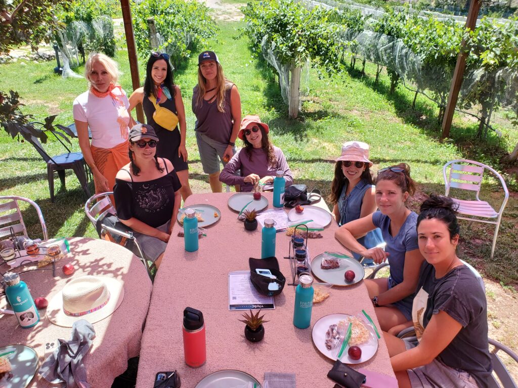 Group of women sitting at a table in a vineyard eating lunch