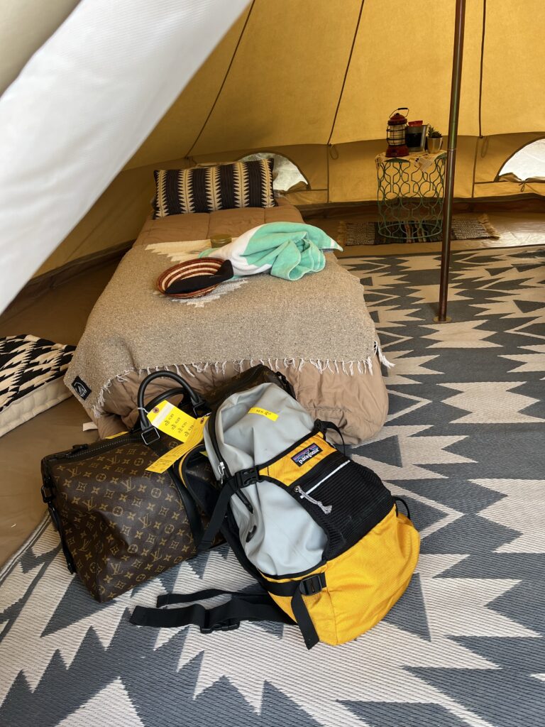Small bed in large luxury tent with bags leaning up against the bottom
