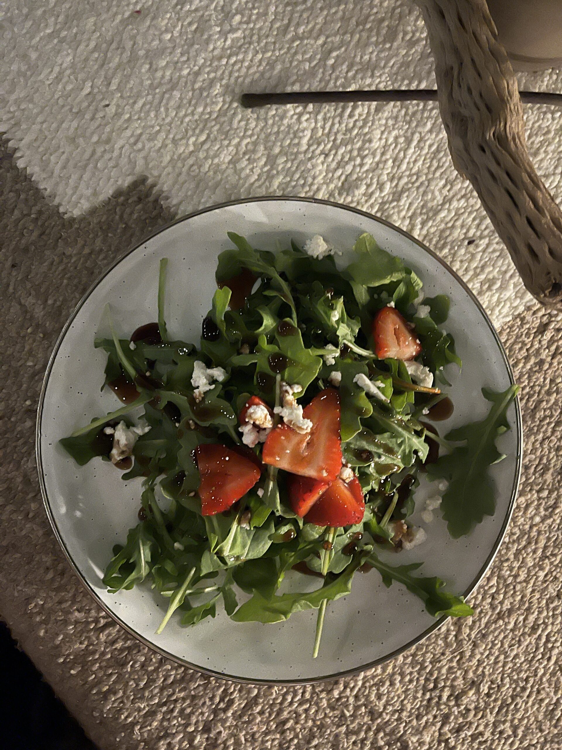 white plate with green lettuce salad and sliced strawberries and feta on top