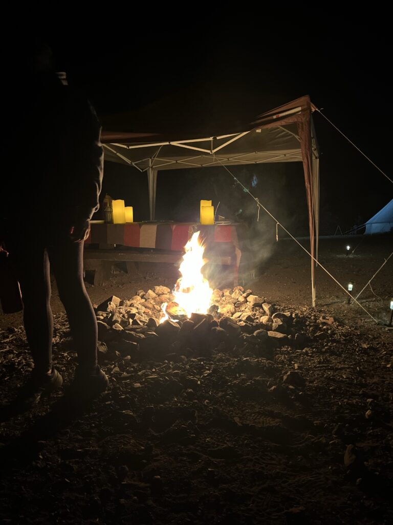 Fire pit made of rocks with fire inside in front of picnic tables and tents