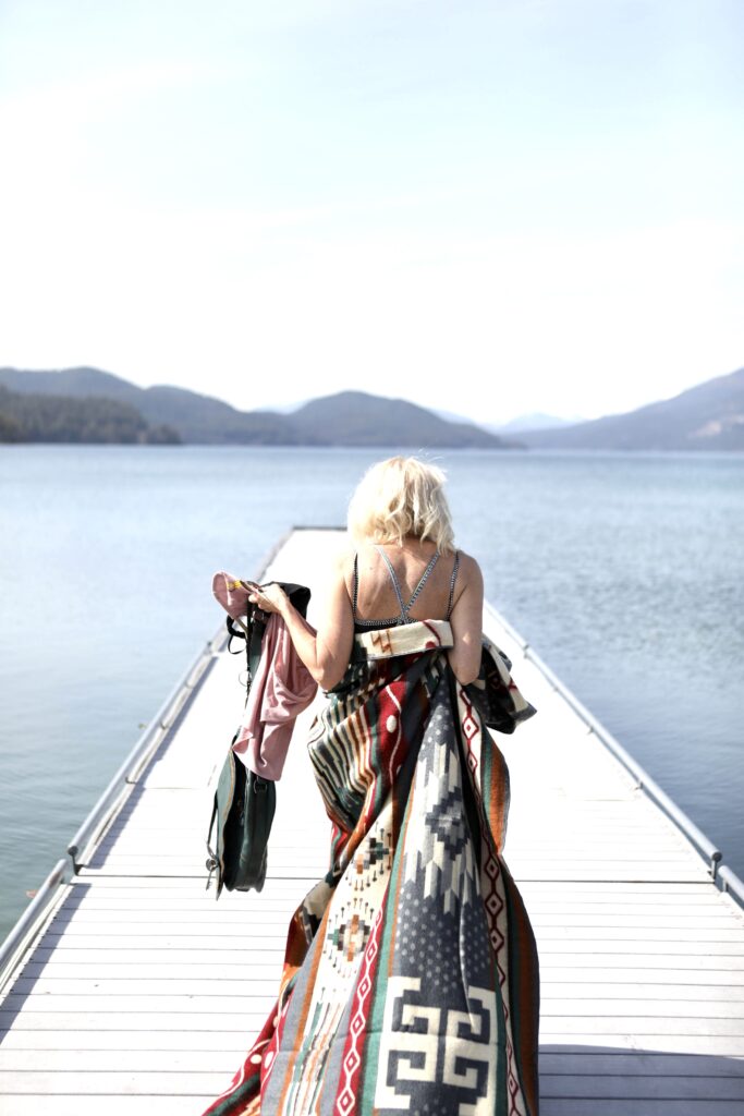 Woman wrapped in a blanket from Ecuadane walking on a long dock on a lake.