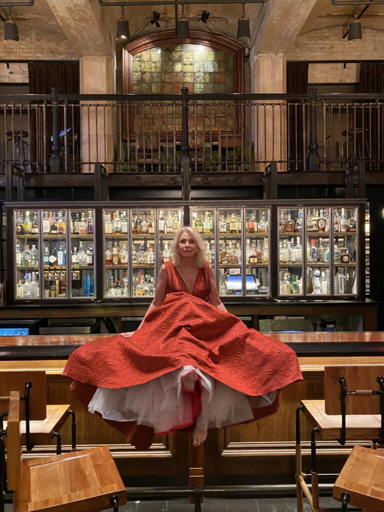 Sonia wearing red gown and sitting on  bar