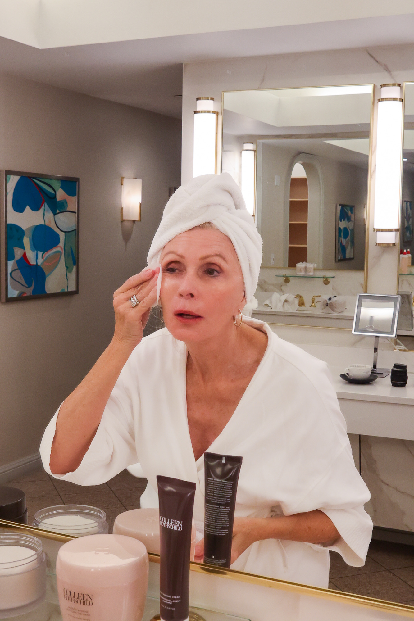 Sonia in a white robe and towel, tending to her skincare in front of the mirrors at The Crescent.