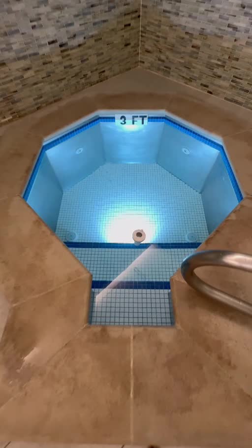 A blue-lit plunge pool with a metal handrail in the tiled spa.